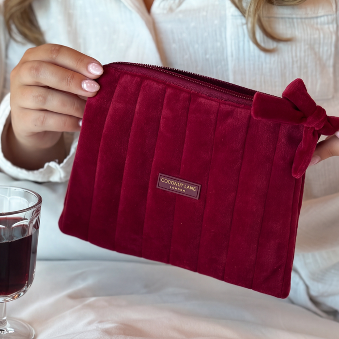 Burgundy velvet cosmetic bag with a quilted design, bow detail, and gold-tone hardware.