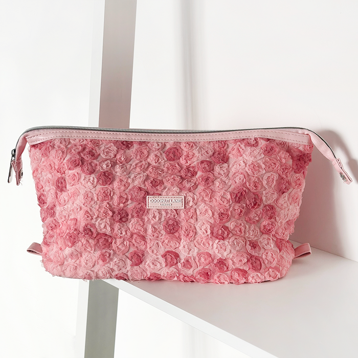 Pink textured Coconut Lane Peony Bloom expandable makeup bag with zipper, displayed on a white shelf.