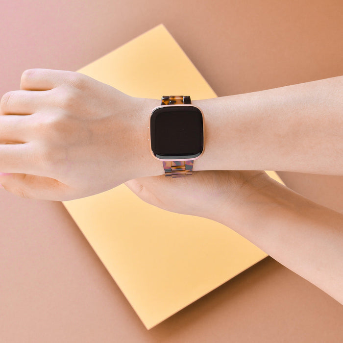 Coconut Lane Luxe Tortoiseshell Fitbit strap on wrist, displayed over a yellow rectangular surface.