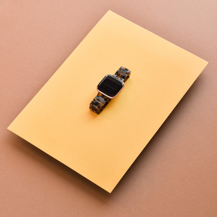 Tortoiseshell-patterned Coconut Lane Fitbit Luxe strap on yellow paper with a brown background.