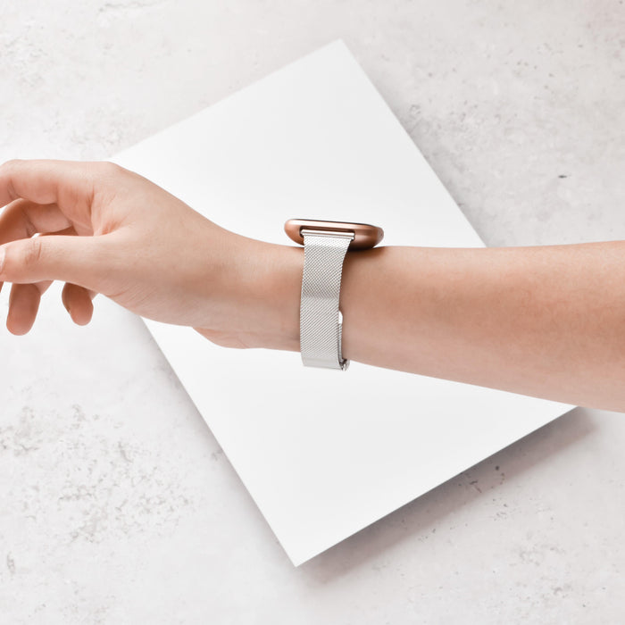 Silver Slim Milanese Coconut Lane Fitbit strap worn on a hand, resting on a white surface next to a blank sheet.
