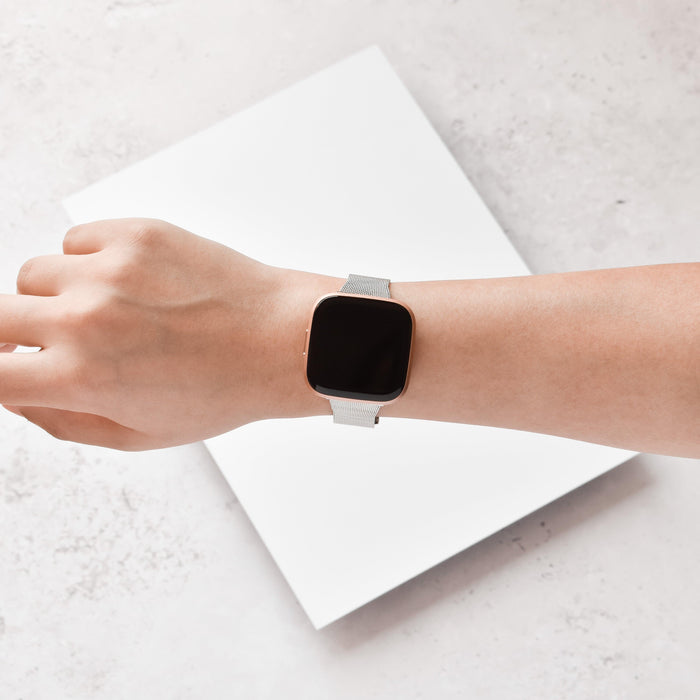 Slim silver Milanese Coconut Lane Fitbit strap on a wrist with a square smartwatch, shown against a white background.