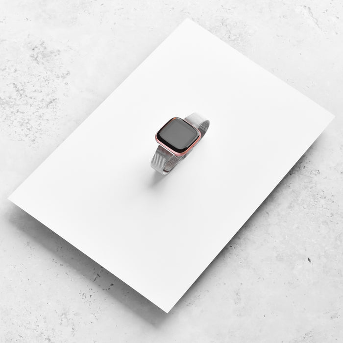 Silver Slim Milanese Coconut Lane Fitbit strap on a white sheet over a light marble background.