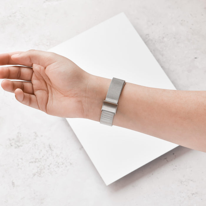 Silver Slim Milanese Coconut Lane Fitbit Strap on wrist, hand resting on a white surface with a white object below.