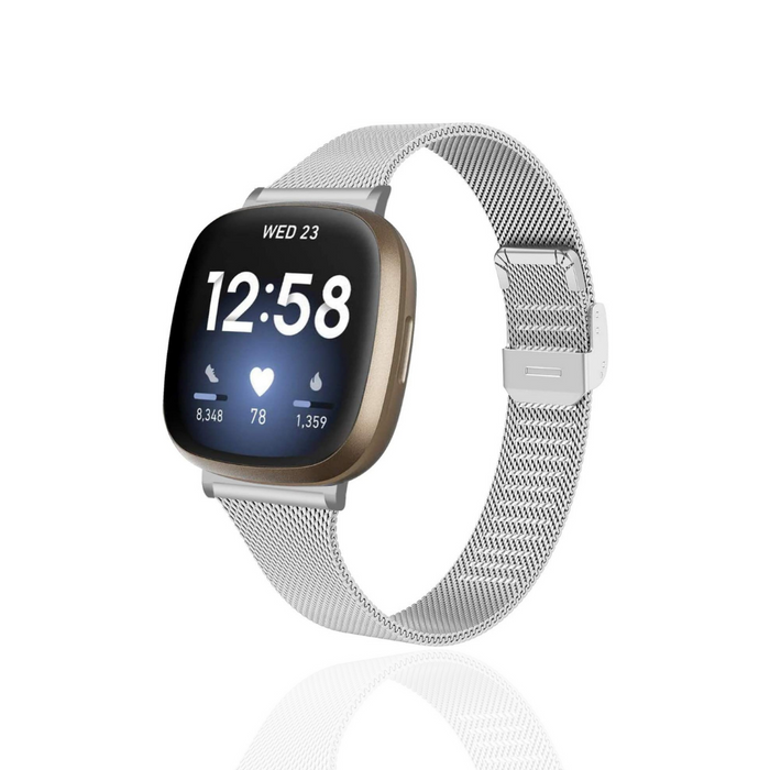Silver smartwatch with slim silver Milanese Coconut Lane Fitbit strap, screen displays time, date, and fitness stats.
