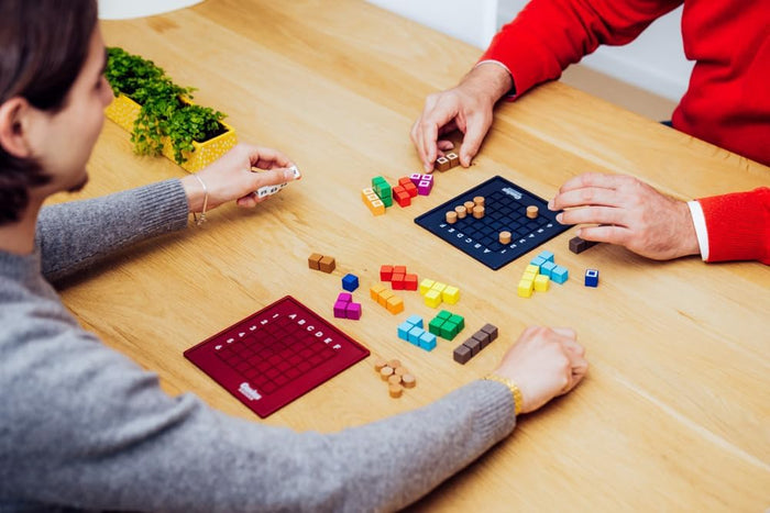 Two people playing with colorful game pieces on a wooden table.