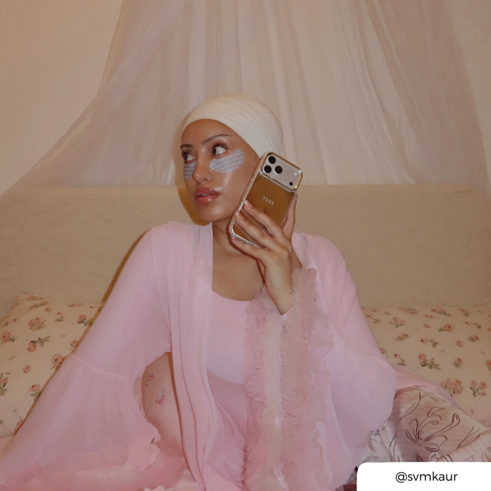 Woman in baby pink gown, holding an phone up to her ear. The phone is in a mirrored cases, with "11:11" text printed on the back.