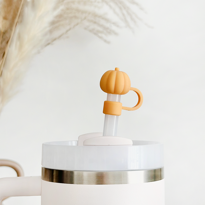 Pumpkin-shaped orange straw cover by Coconut Lane on a clear tumbler with straw, set against a soft neutral background.