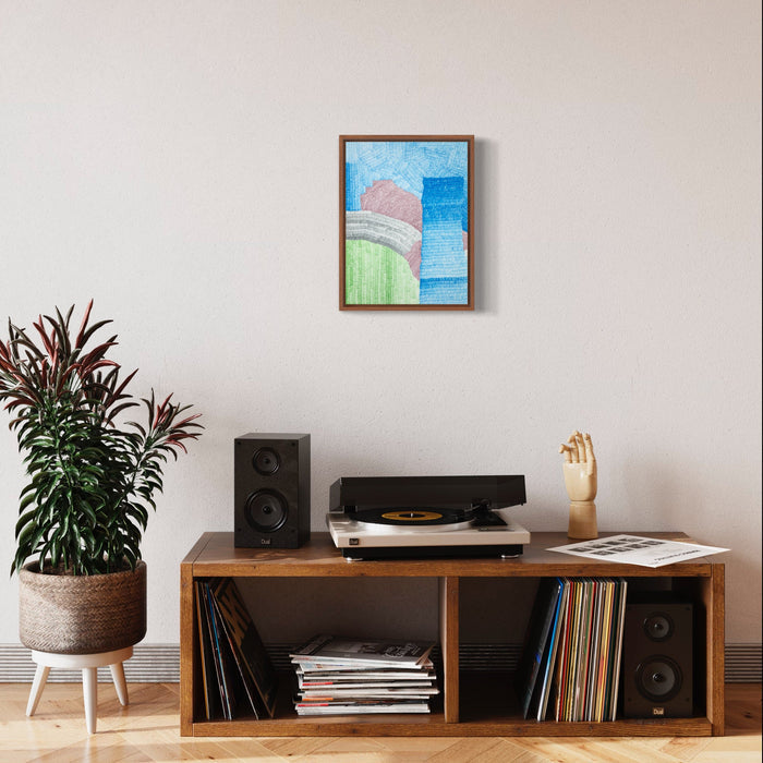 The artwork 'Still' by Lynnette Therese Sauer features abstract geometric shapes in soft pastel colors. A gentle pink curved form rests against a mint green horizontal element, set against a graduated blue sky background. The ink on paper piece is displayed in a brown wooden frame, creating a serene, minimalist composition measuring 16 x 12 inches by Lynnette Therese Sauer.