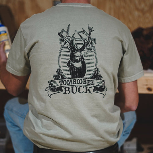A person wearing a beige t-shirt with 'TOMBIGBEE BUCK' written on it and a graphic of a deer with antlers.