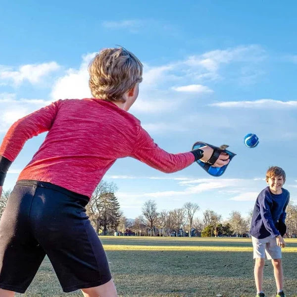 Two children playing with a ball on a grassy field under a blue sky.